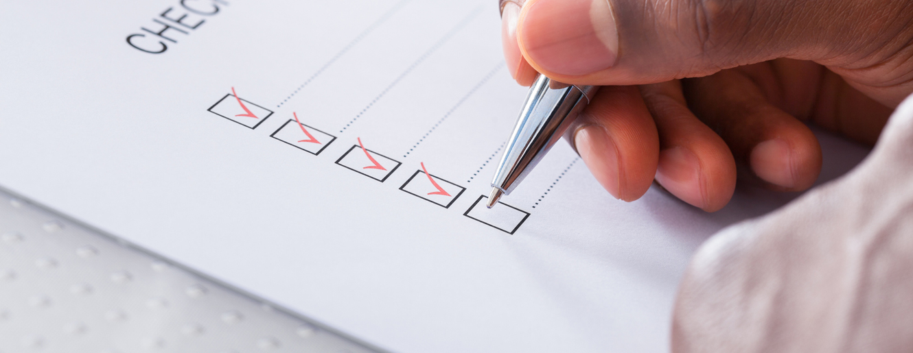 Hand holding pen beside checklist written on paper.